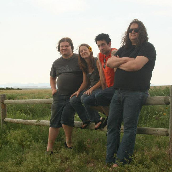 A photo of the band Out On Bail sitting on a wooden fence in a field of grass.