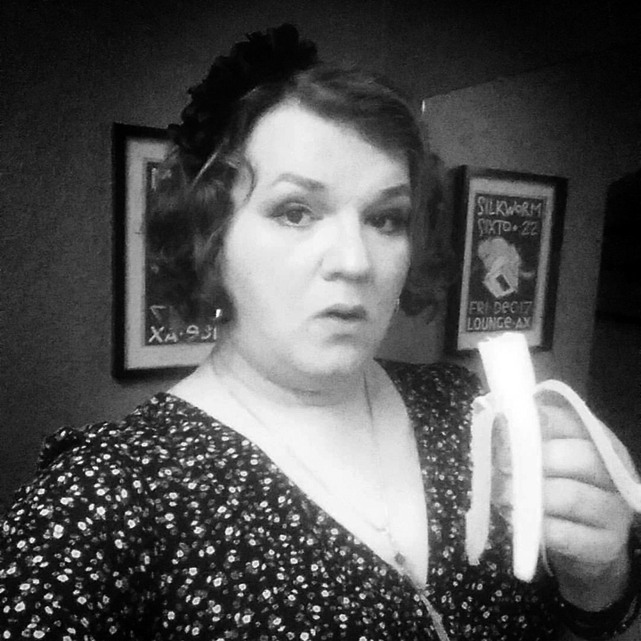 A picture of Josie Cool dressed as a 1930s film Noir actress, holding a half eaten banana.