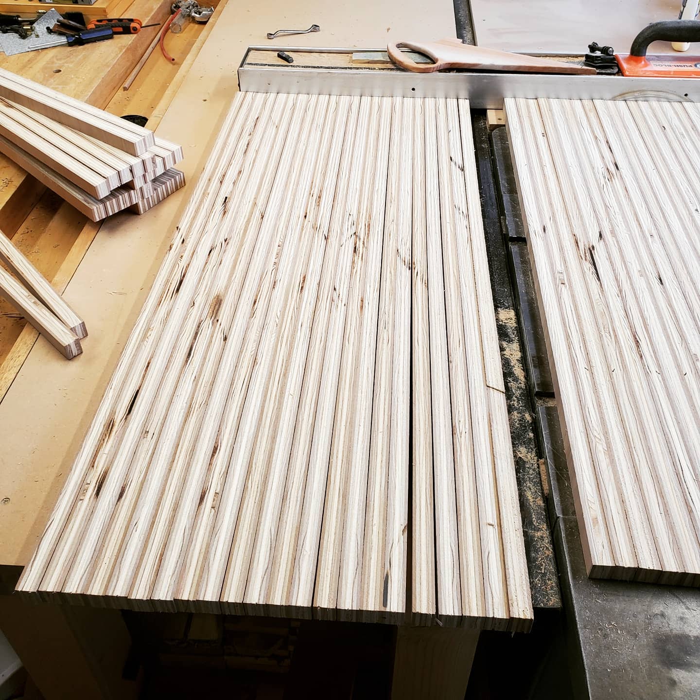 Strips of Cherry plywood lined up on top of a table saw to be glued together.