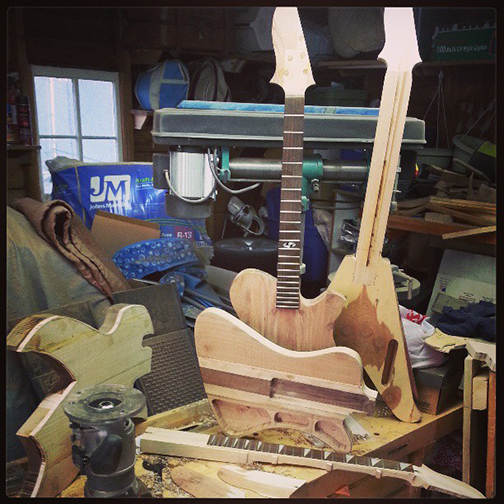 An image of multiple guitars in the process of being built. The guitars are siting on top of a workbench inside my woodworking shop.